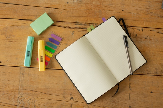 An open notebook, a pen, two parkers, and post it notes